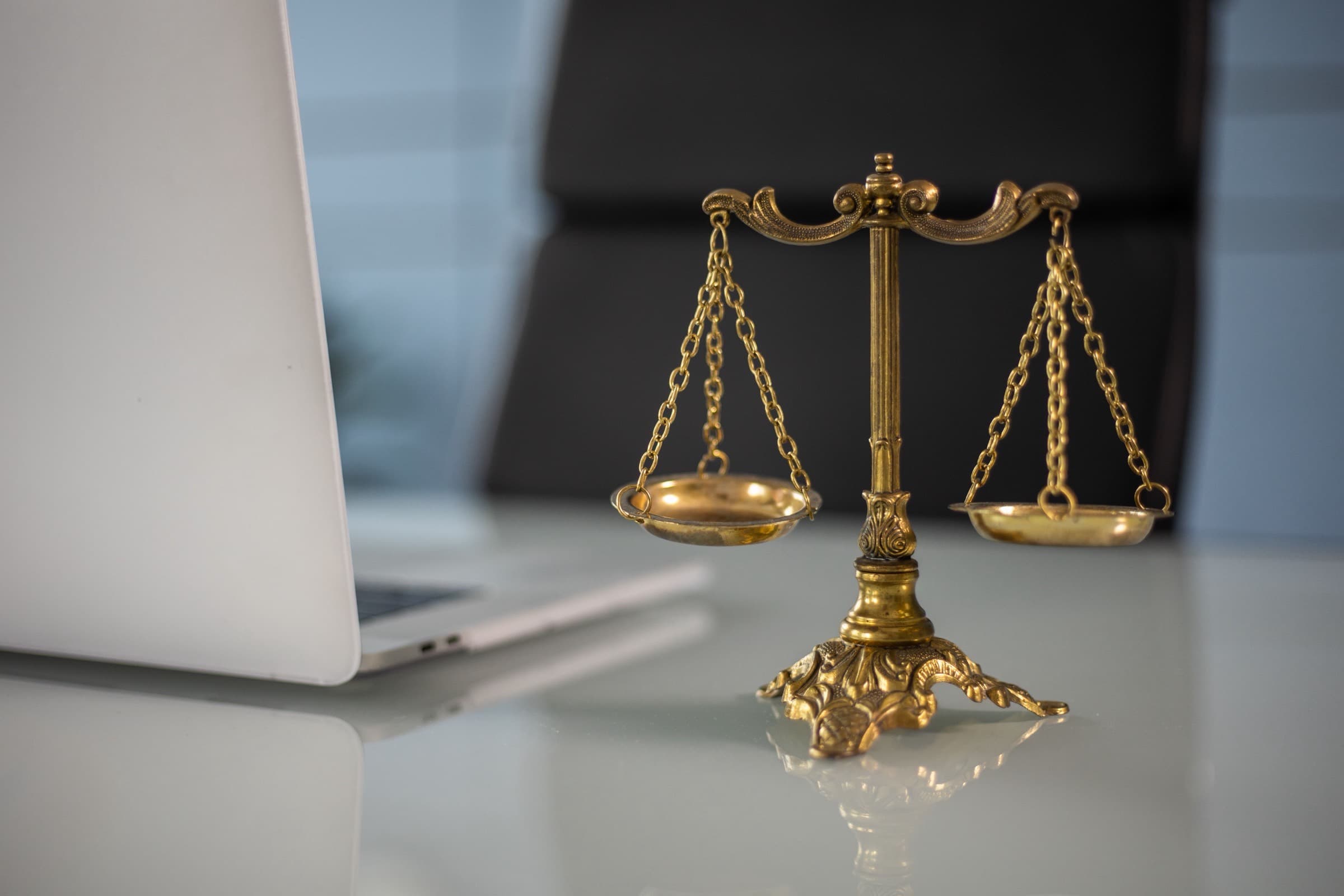 Brass set of scales of justice on a white desk beside an open laptop in a law firm office