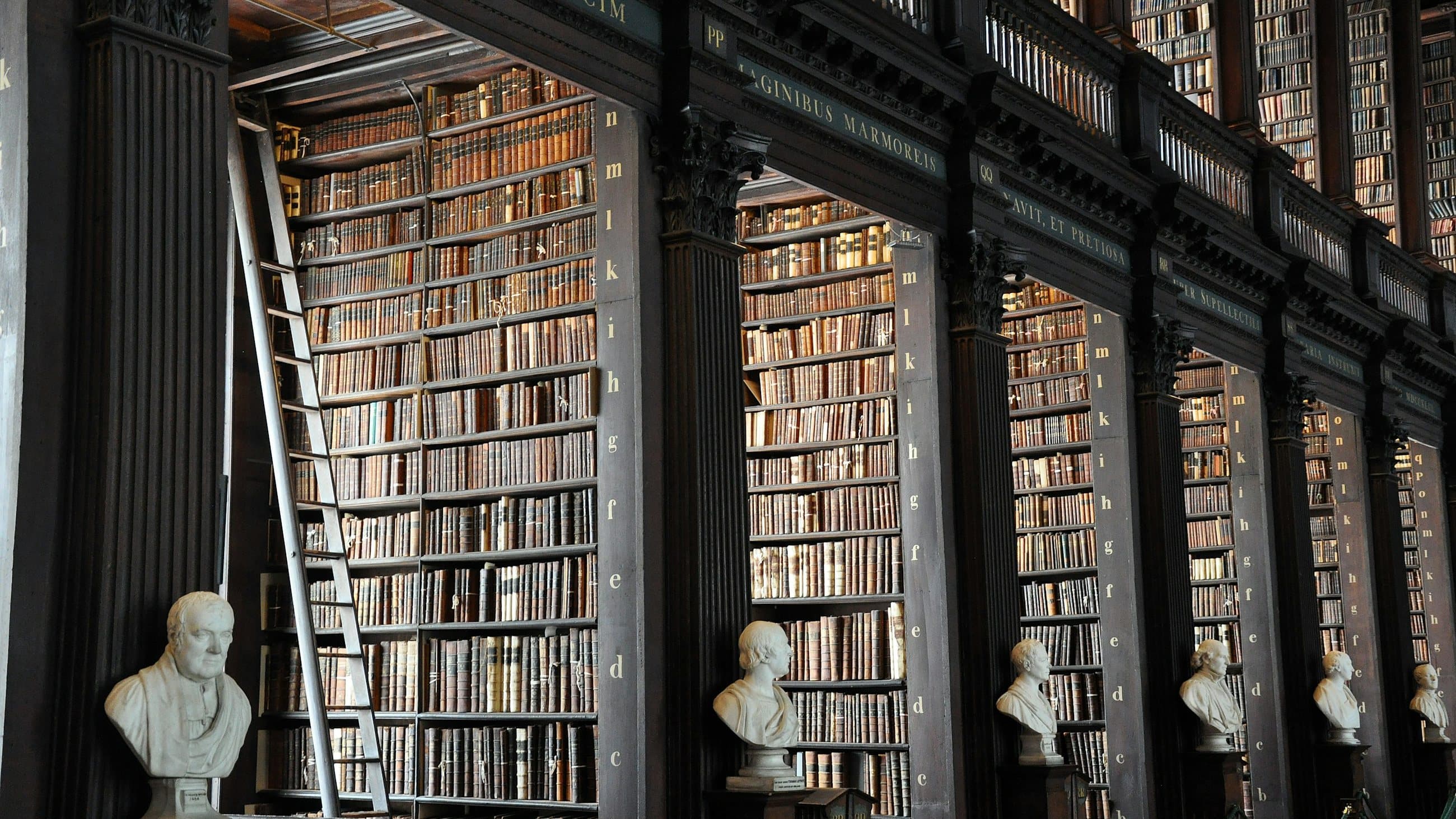 A panelled law library lined floor to ceiling with bound volumes, marble busts along the aisle and a rolling ladder against the shelves