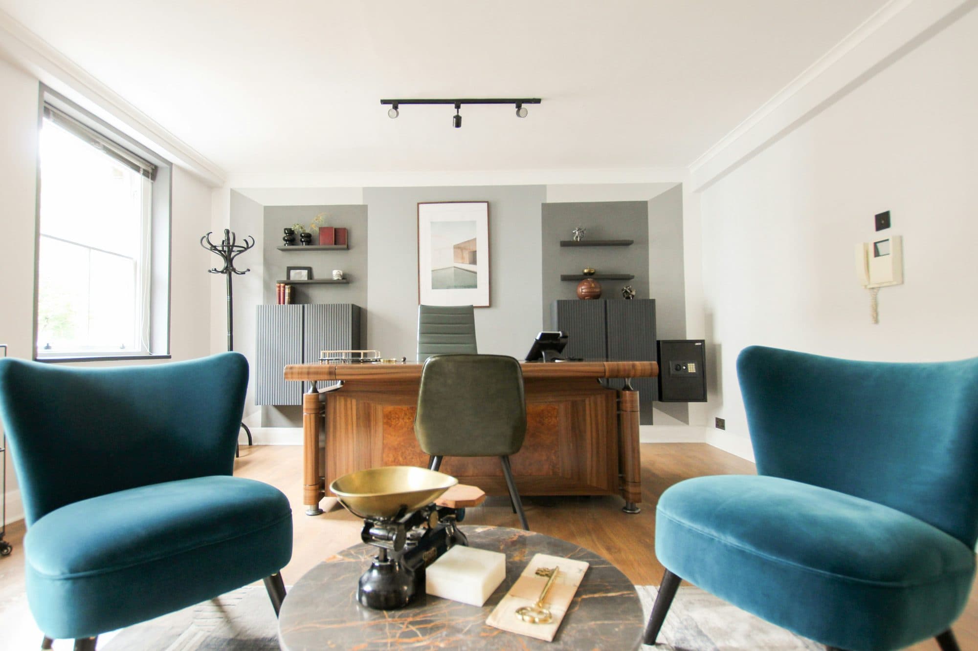 A pair of teal velvet armchairs facing each other in a bright London consulting room with tall sash windows