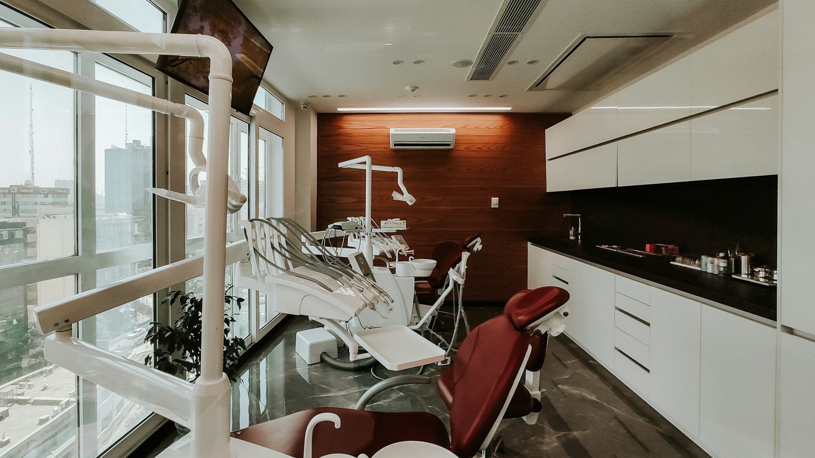 A calm, modern dental surgery with a burgundy treatment chair and warm wood panelling