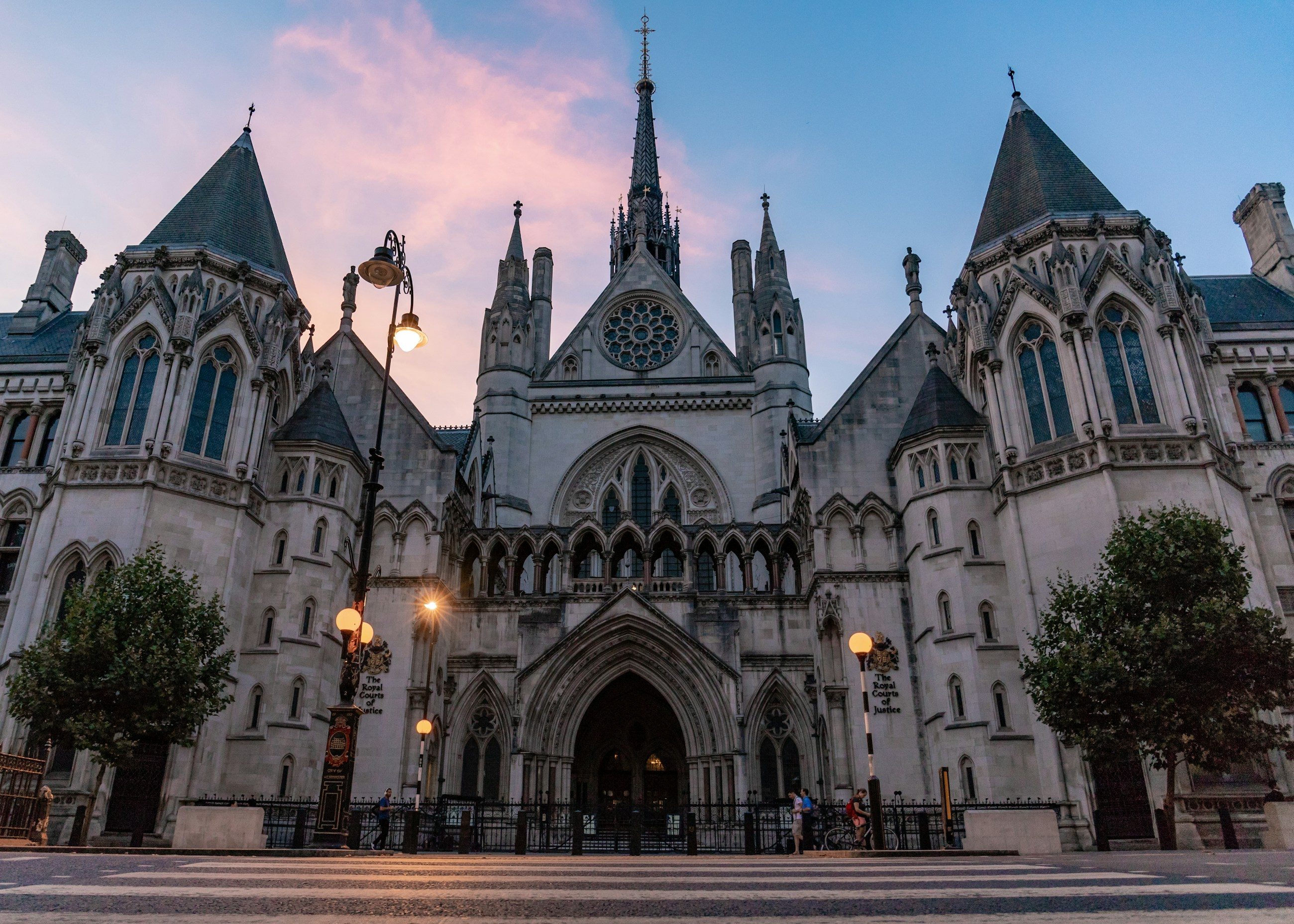The Strand front of the Royal Courts of Justice in London at dusk, with its lamps lit