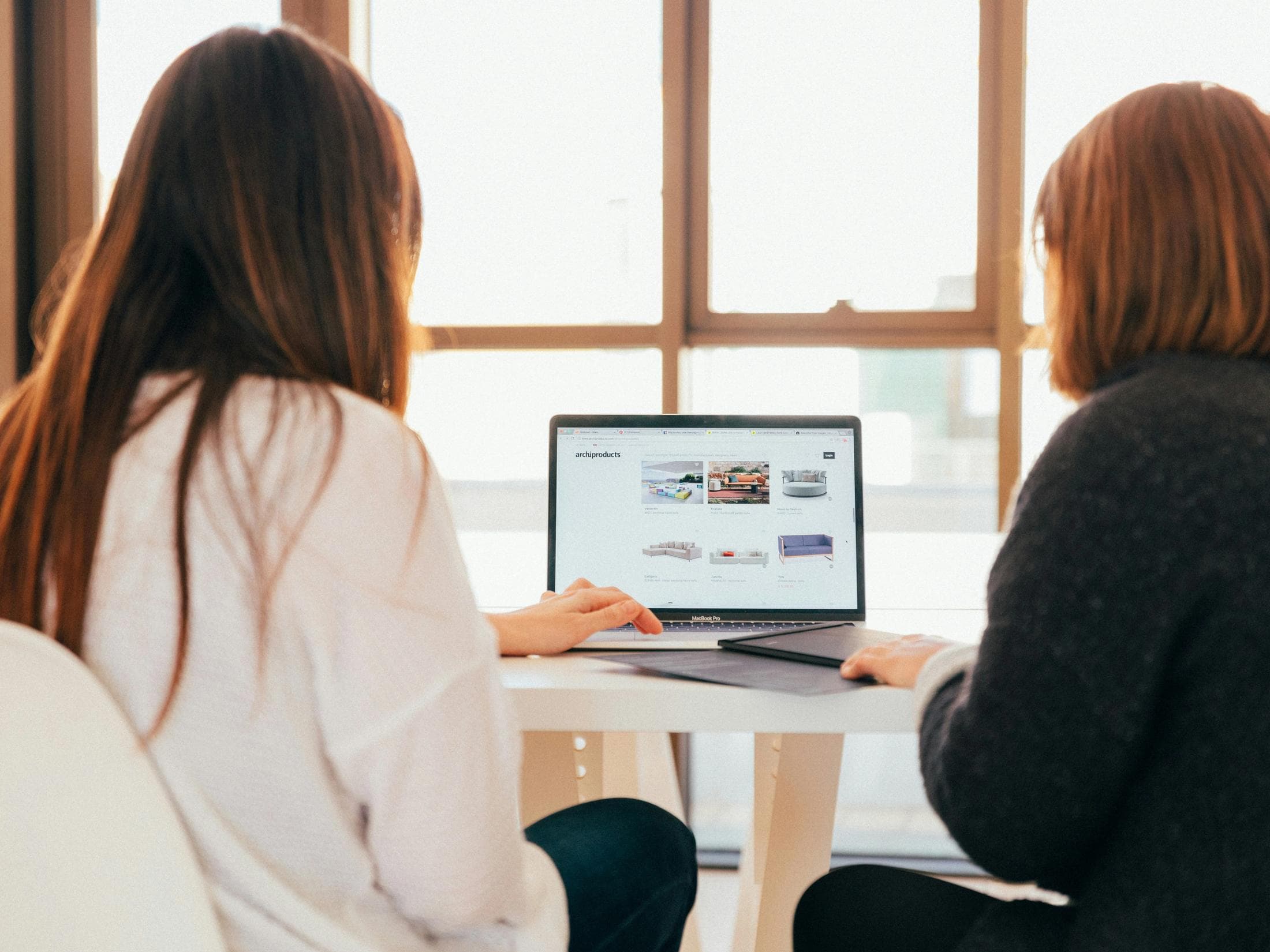Two people reviewing a website together on a laptop at a sunlit desk.