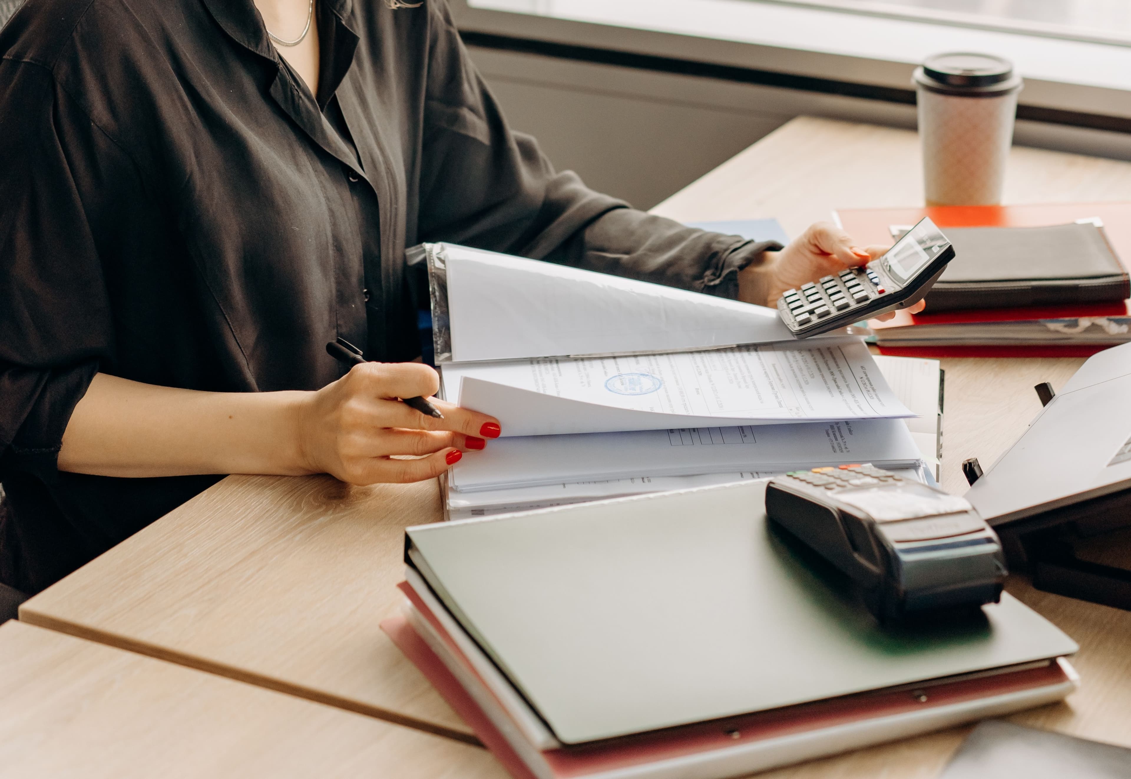 Accountant at a desk reviewing figures on a laptop and paperwork, calculator and notes to one side, in a small practice office