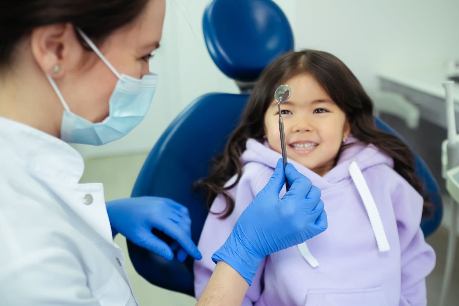 A dentist checking a young girl's teeth with a mirror