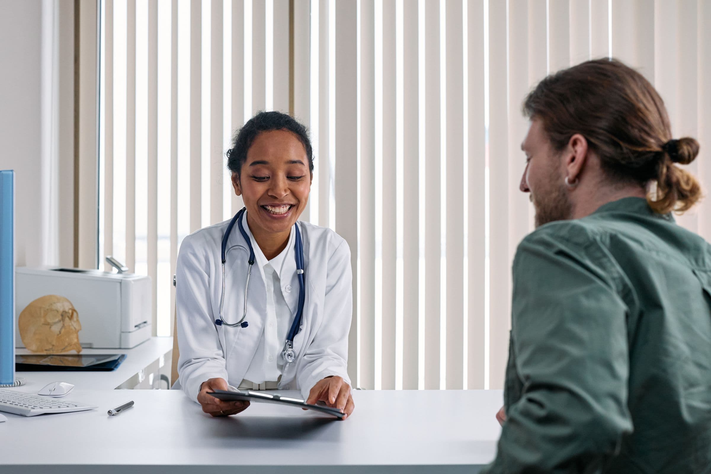 A private GP smiling with a patient across a bright consulting room desk, sharing notes on a tablet