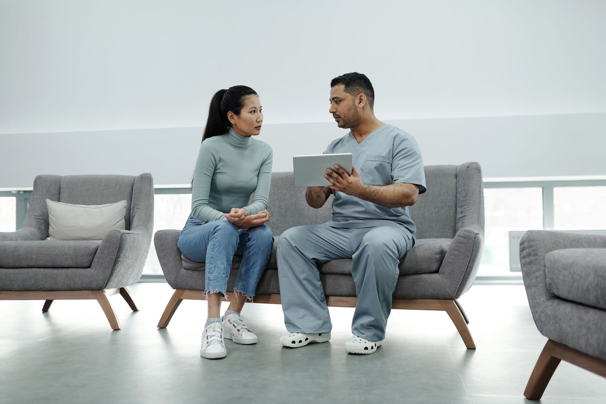 A private doctor and patient talking through options on a tablet in a calm, bright clinic seating area