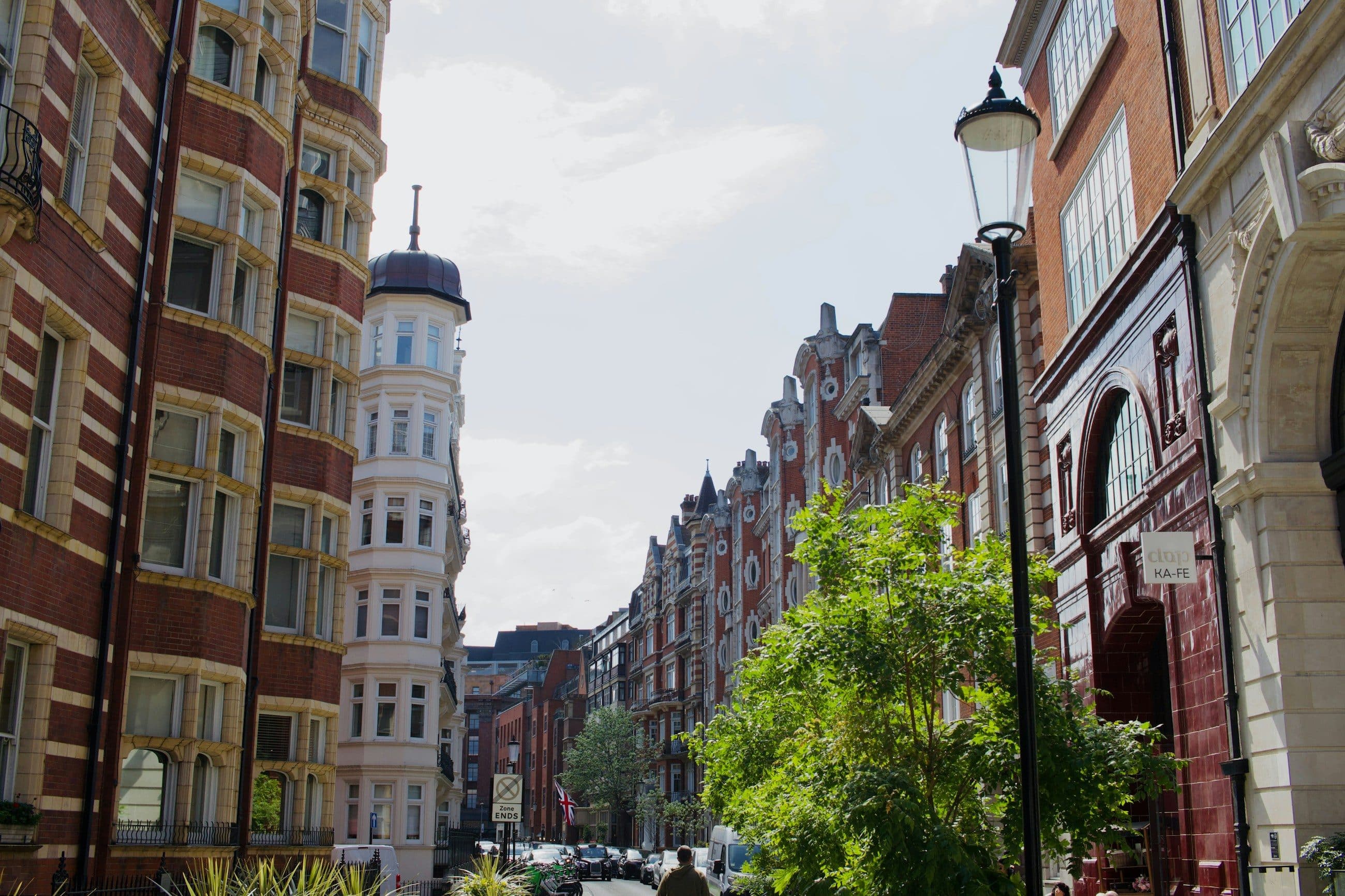 A tree lined London street of red brick mansion blocks in afternoon light