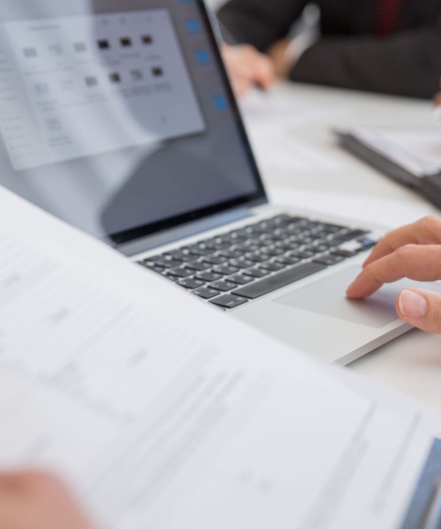 A printed proposal being read at a desk beside an open laptop