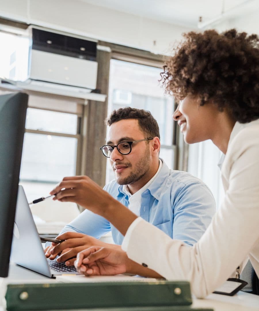 A smiling woman pointing out something on a laptop screen to a business owner beside her