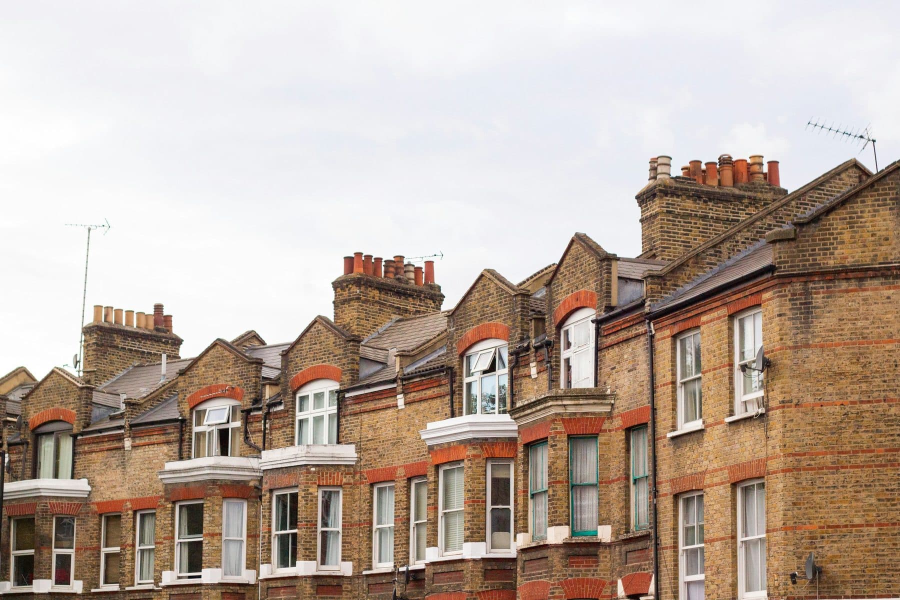 A row of yellow brick Victorian terraced houses in London with red banding and chimney pots