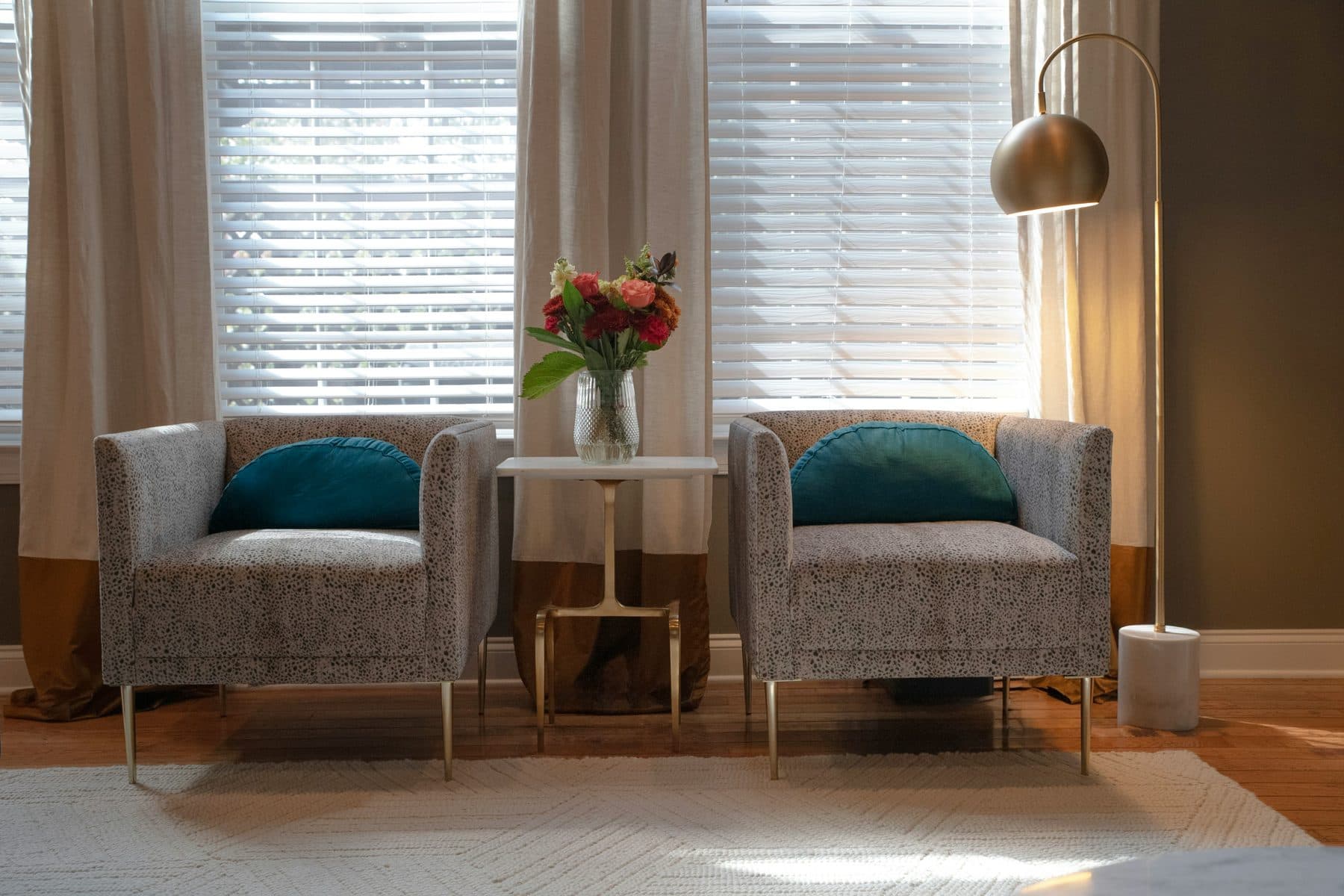 Two upholstered armchairs facing each other by a shuttered window, with flowers on a small side table between them