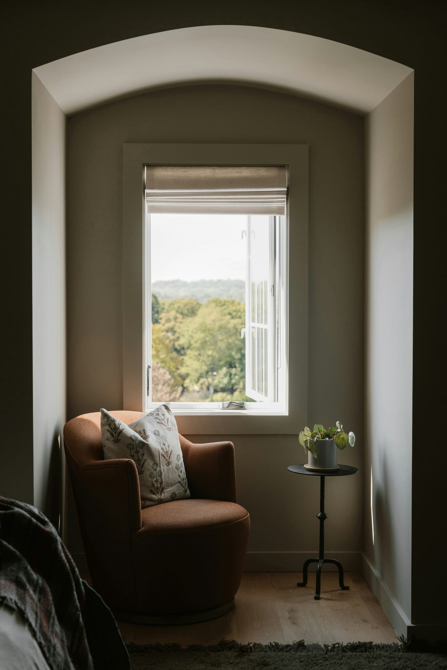 A small armchair in a quiet alcove beneath a window with a view over trees