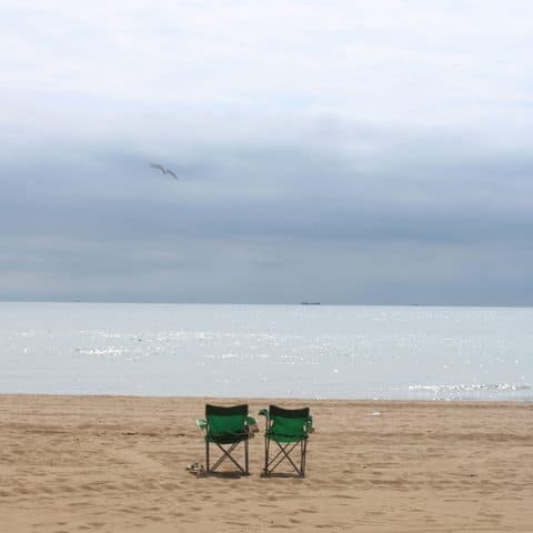 Two empty folding chairs on the sand at Broadstairs, facing a calm grey sea