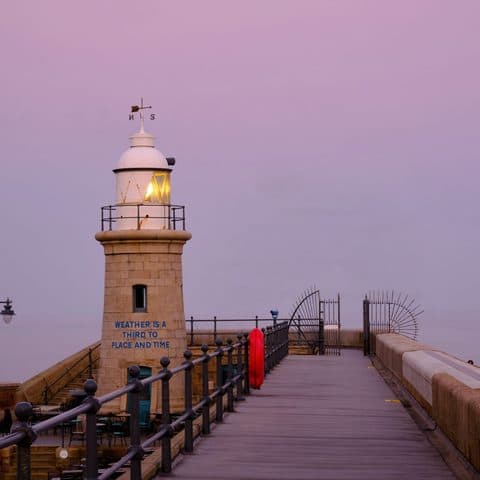 The lighthouse at the end of Folkestone Harbour Arm under a soft pink sky at dusk