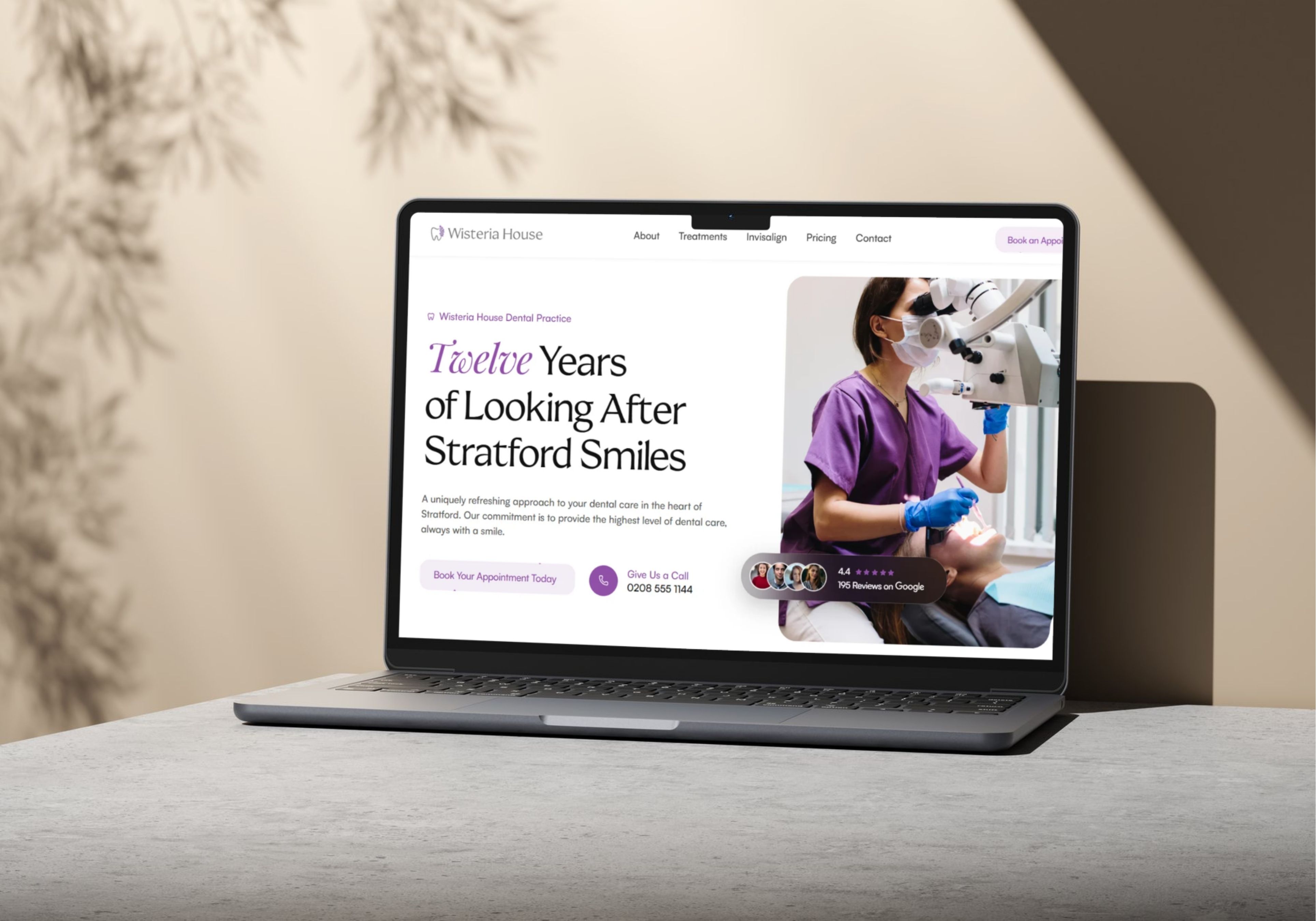 Redesigned East London dental practice homepage on a laptop, photographed on a marble desk with soft foliage shadows
